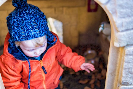 A young boy in woolly hat inside a playhouse in the nursery’s garden.